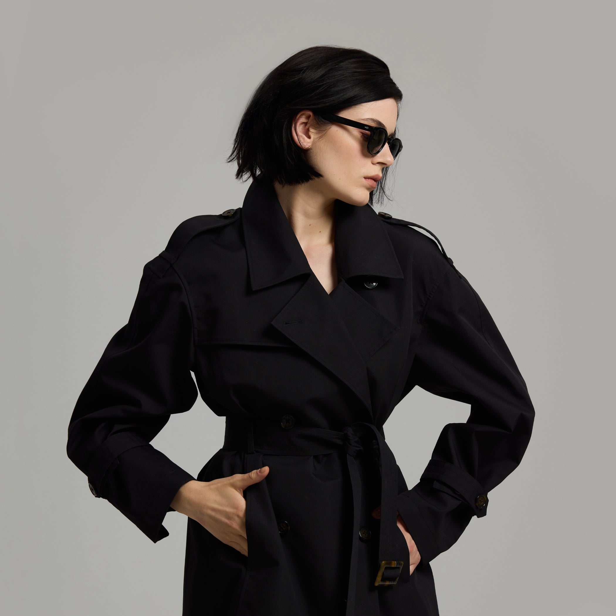 Person wearing a black trench coat on a gray background